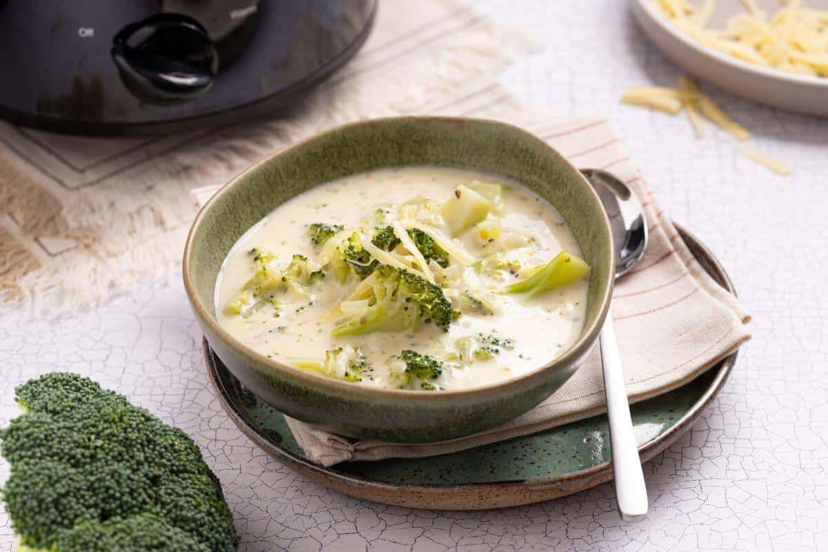 A bowl of soup with broccoli and cheese on a plate.