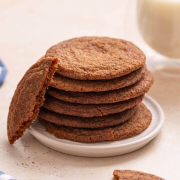 A stack of brown sugar cookies on a plate next to a glass of milk.