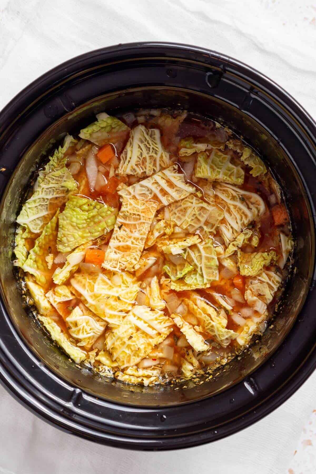 A crock pot filled with broth and vegetables.