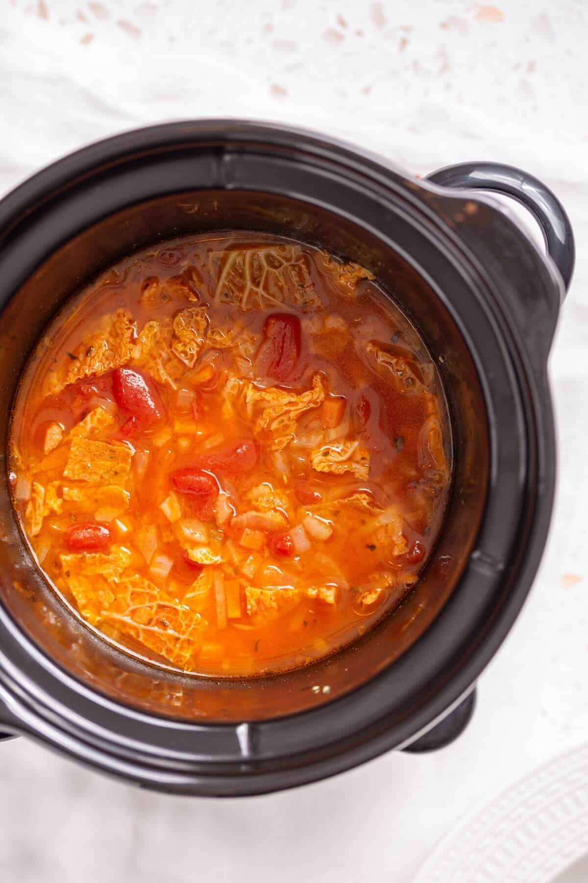 A crock pot full of cabbage soup on a table.