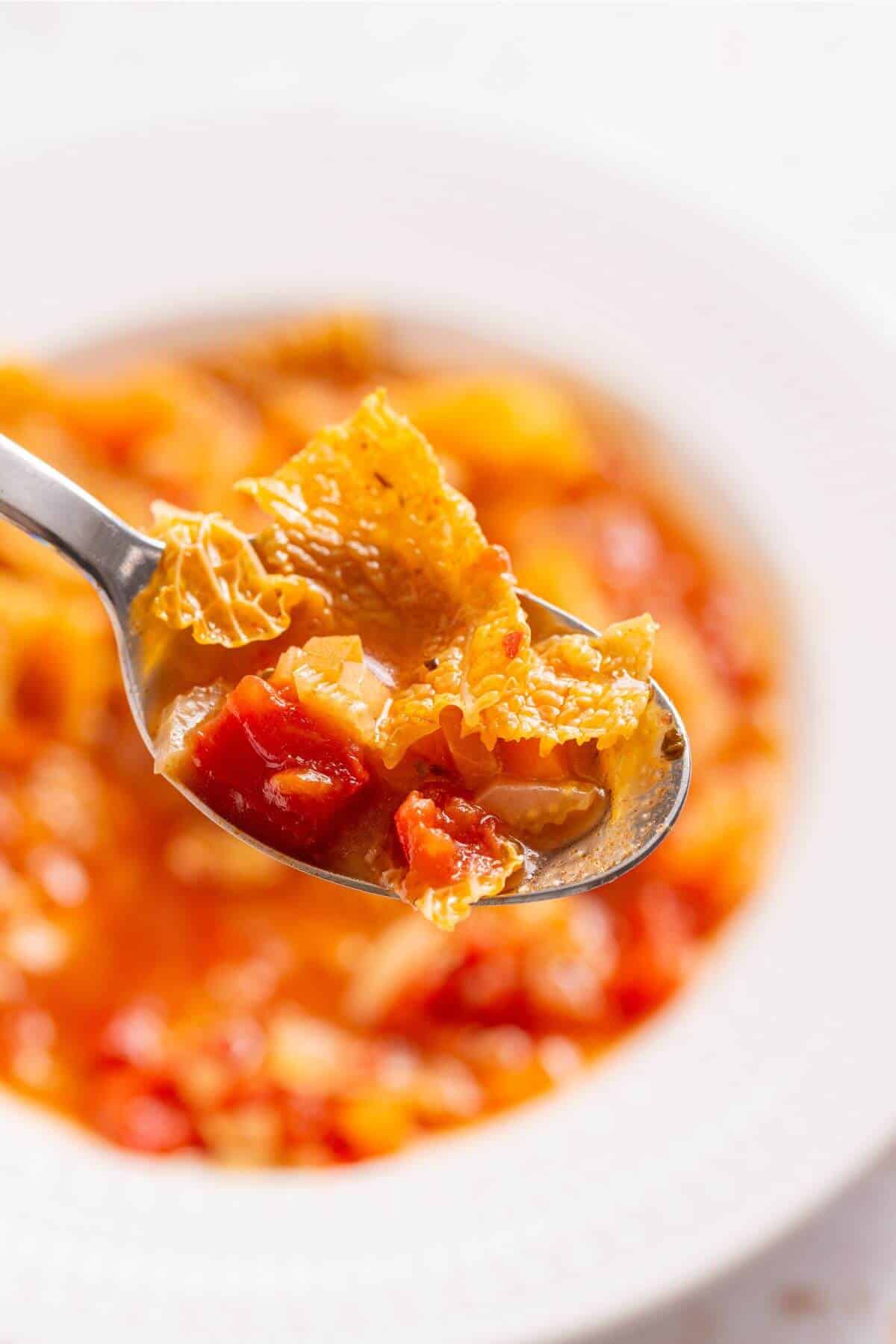 A spoonful of cabbage soup is held over a bowl of soup.