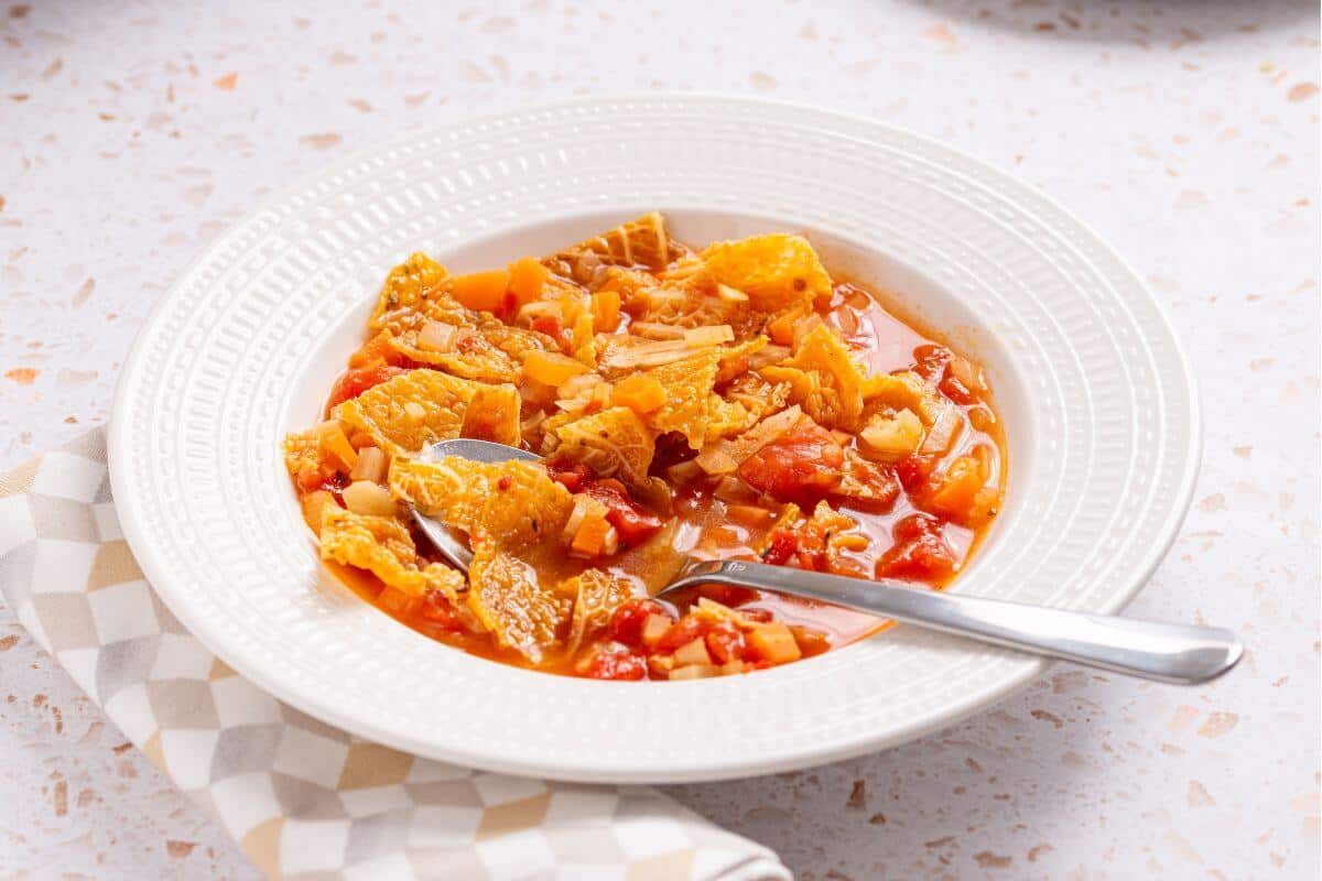 A bowl of soup with cabbage and tomatoes on a table.