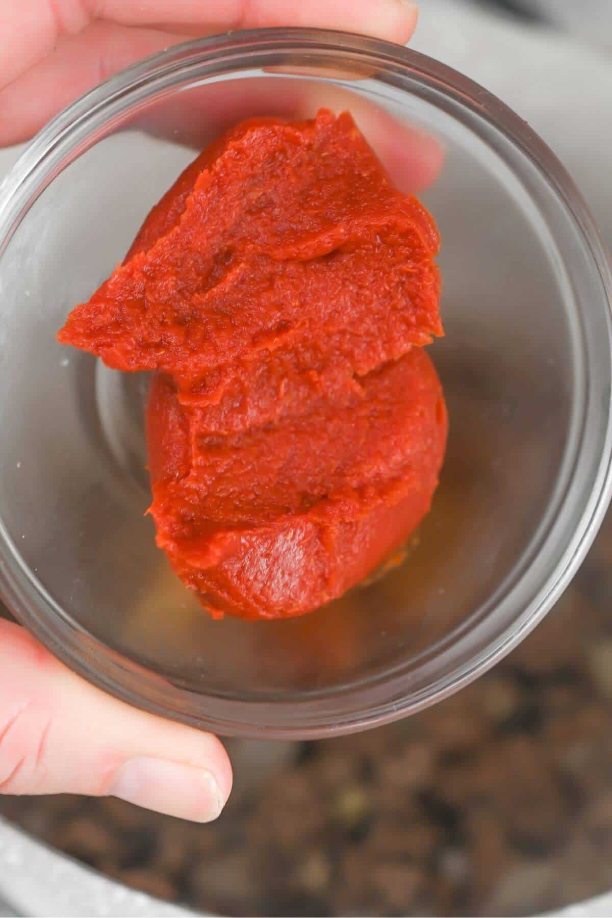A person holding a bowl of red tomato paste over browned ground beef.