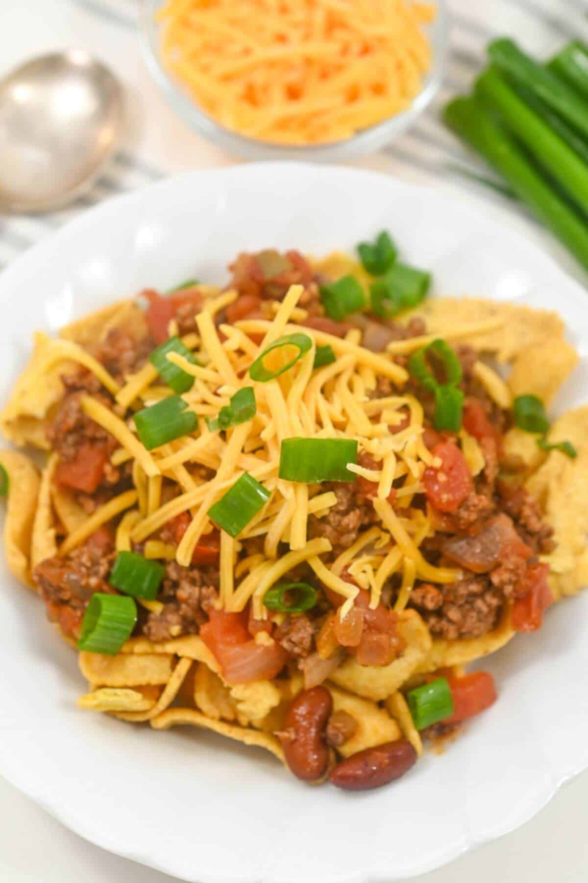 A plate of Frito chili pie topped with green onions and meat.