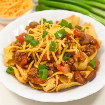 A plate of Frito chili pie with green onions and cheese.