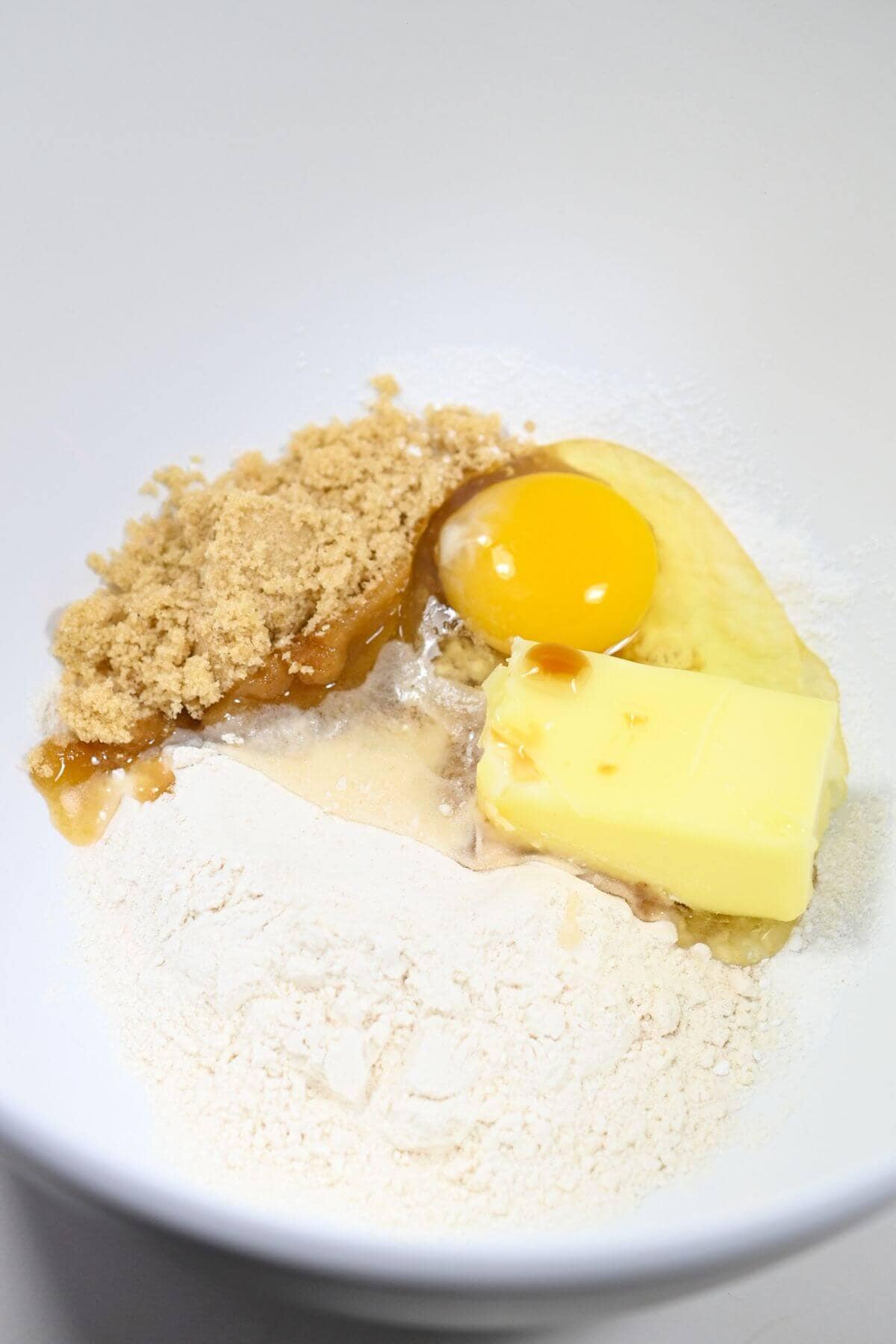 A bowl of ingredients with an egg, flour, butter, and brown sugar.