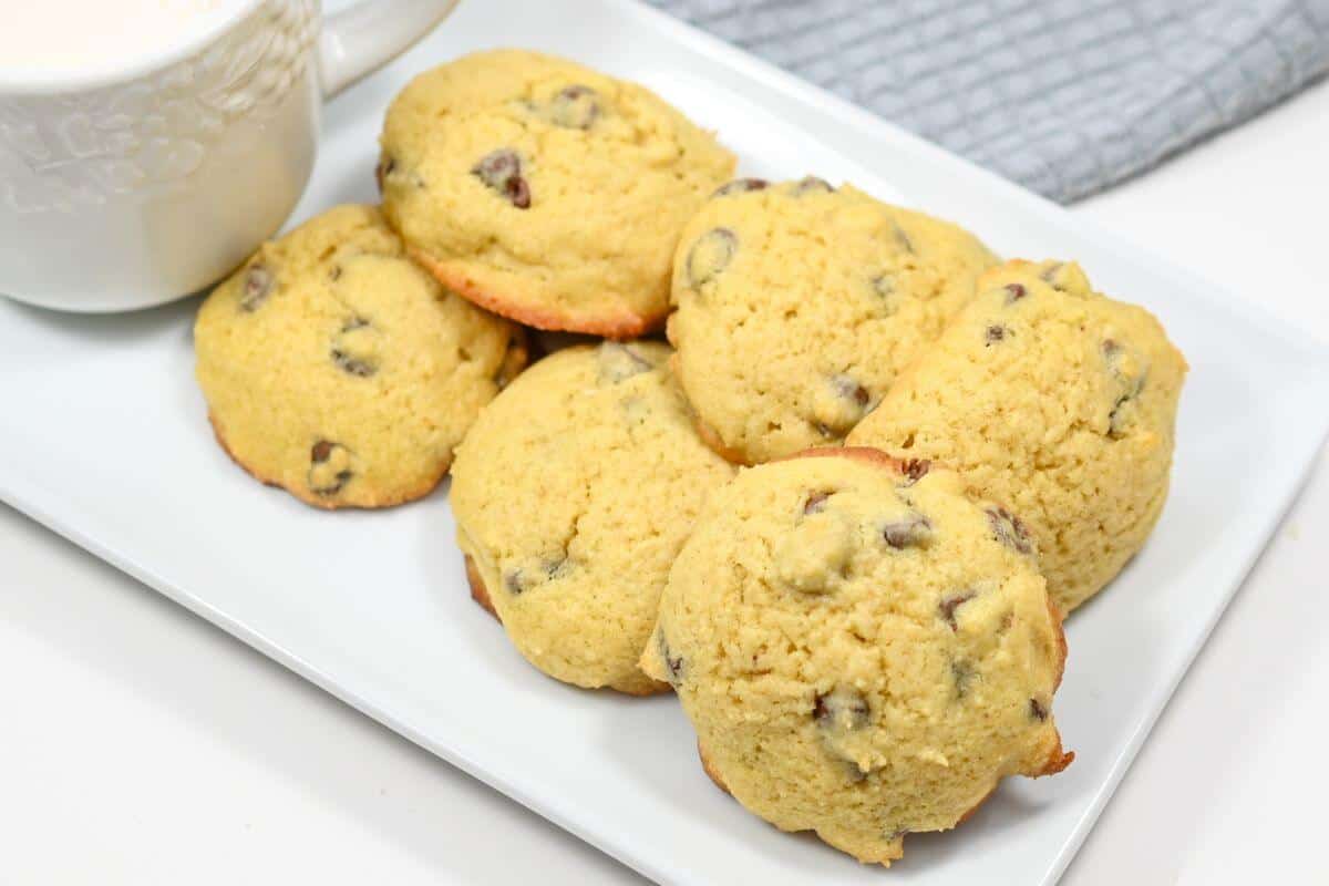 Chocolate chip cookies on a white plate with a cup of milk.