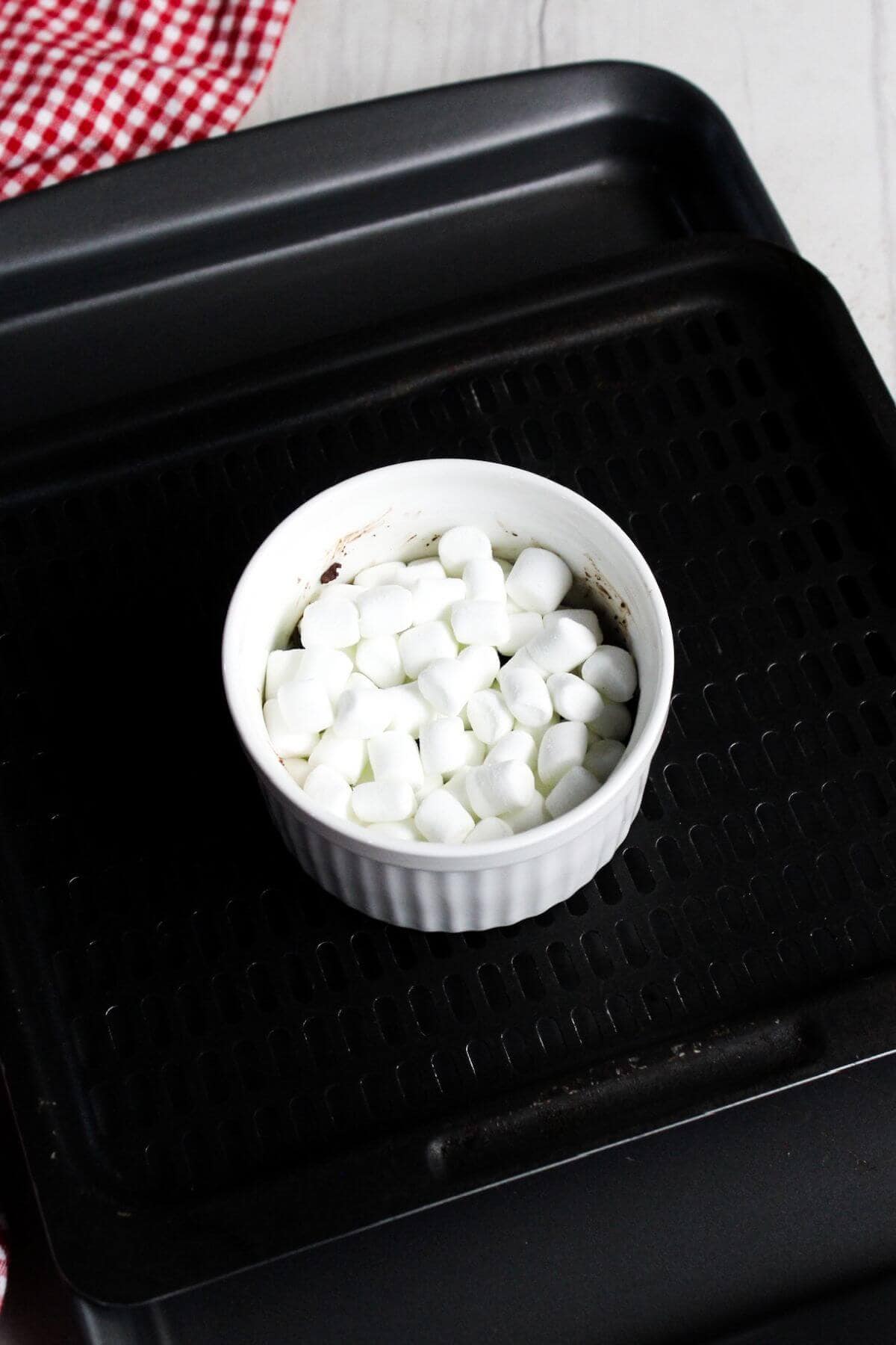 Marshmallows in a ramekin on an air fryer tray.