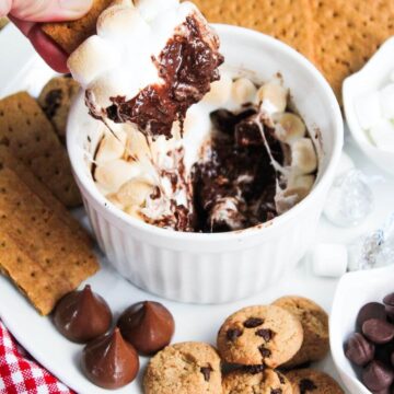 A person is dipping a graham cracker into a bowl of chocolate smores dip.
