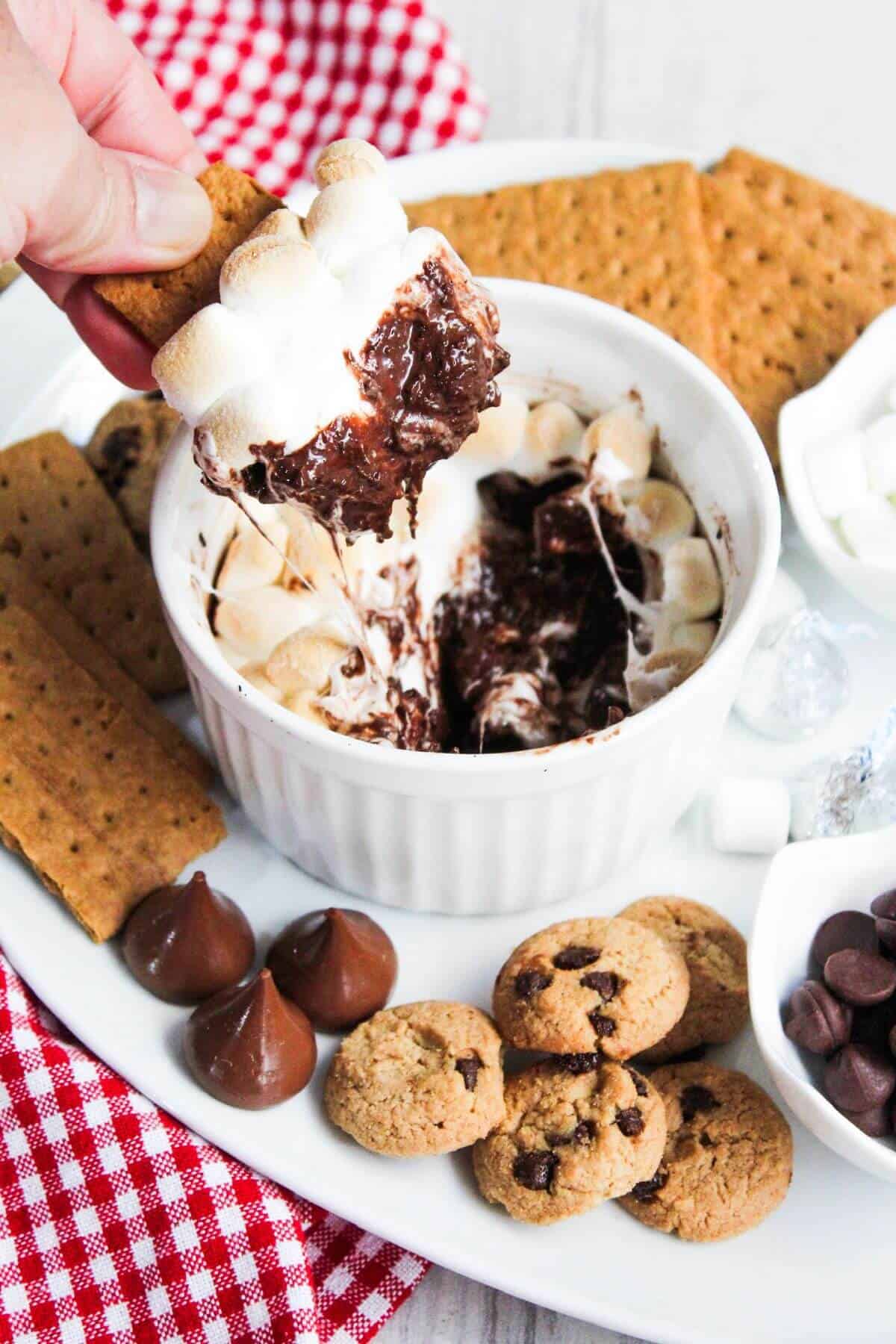 A person is dipping a graham cracker into a bowl of chocolate smores dip.