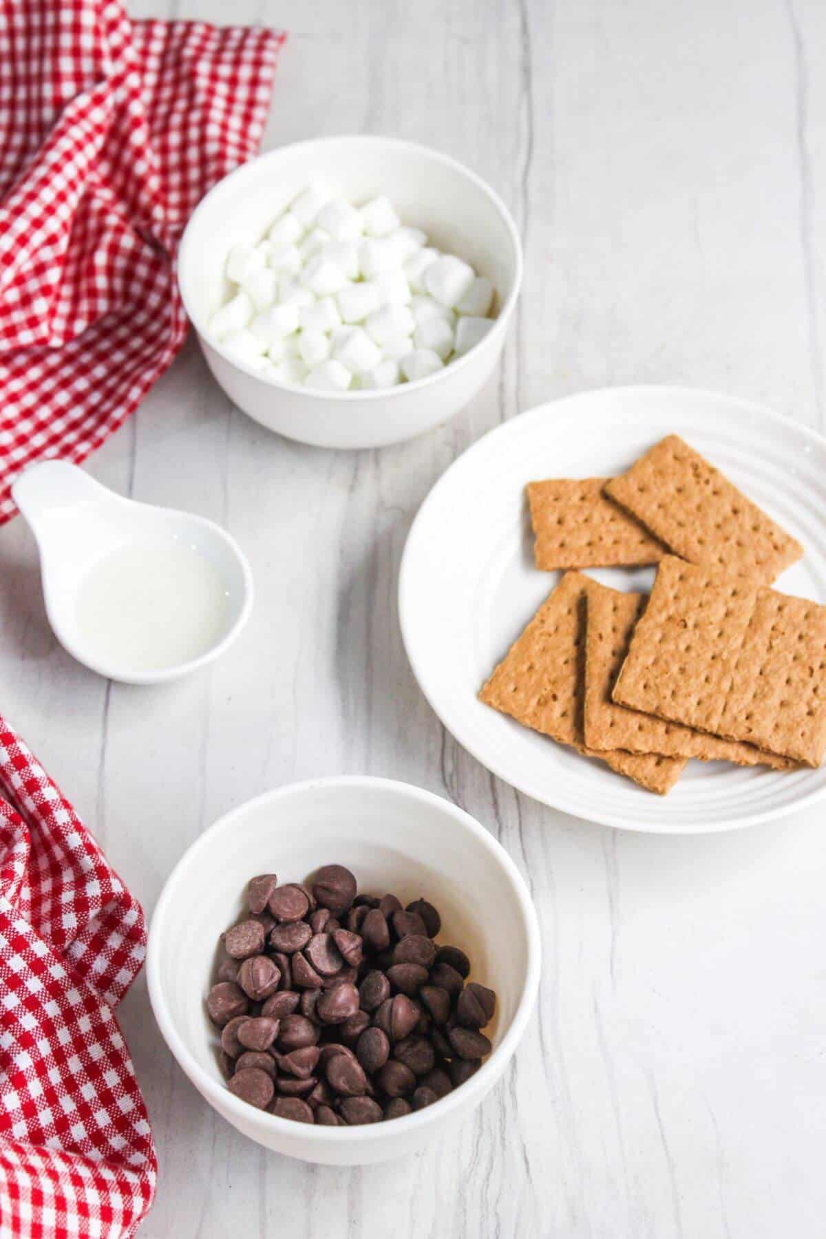 Graham crackers, chocolate chips and marshmallows on a white table.