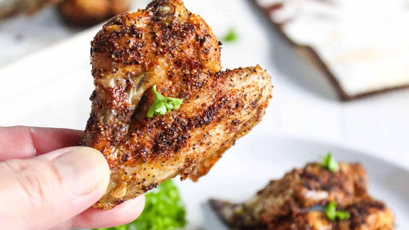 A person holds a seasoned, air-fried chicken wing garnished with parsley.
