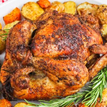 Roasted chicken with potatoes and carrots on a white platter, garnished with rosemary.