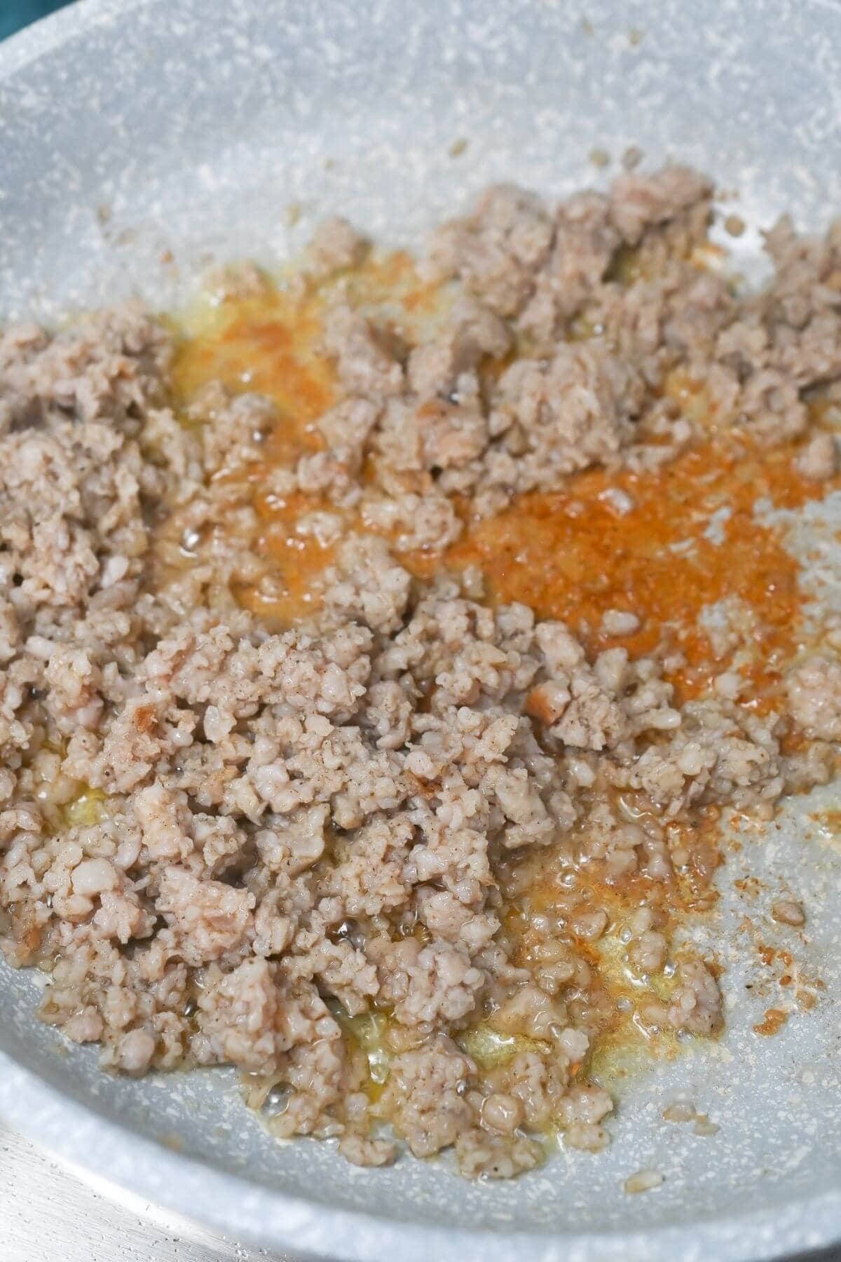 Ground sausage cooking in a pan with oil.