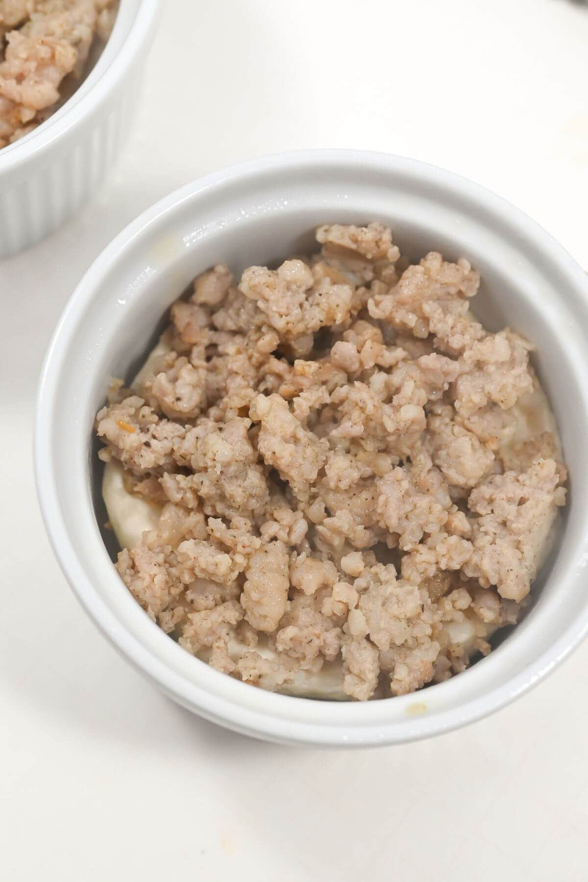 A ramekin with biscuit dough and cooked ground sausage.