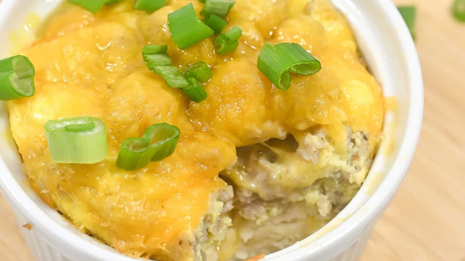 Steamed egg dish topped with melted cheese and garnished with chopped green onions, served in a white bowl.