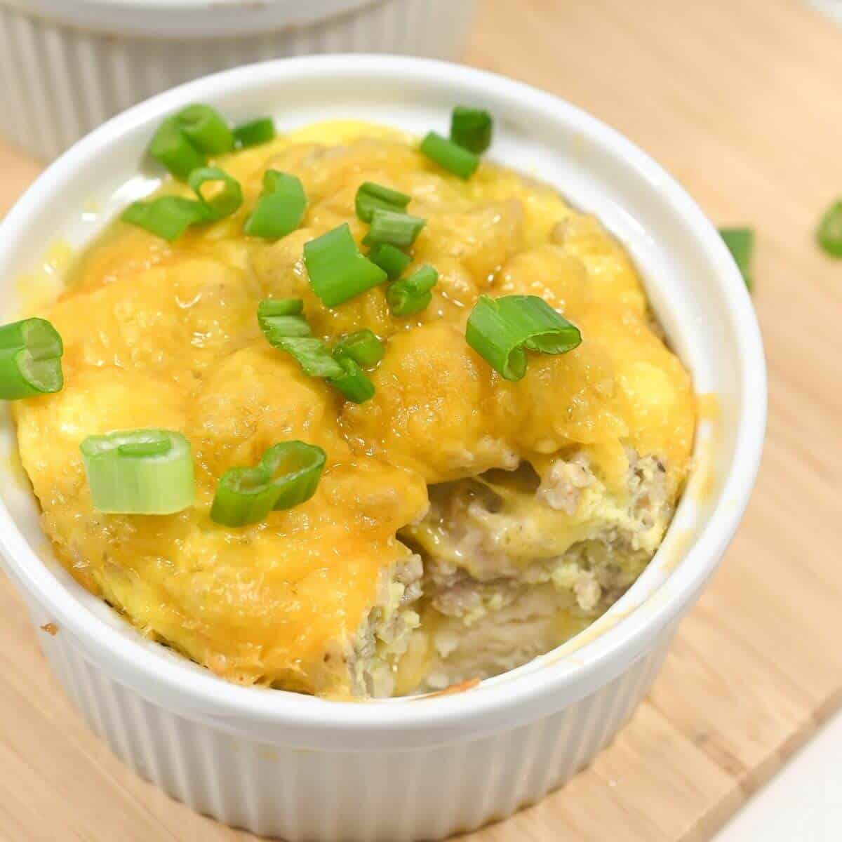 Cheese-topped breakfast casserole garnished with green onions in a white ramekin.