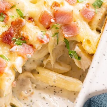 Creamy baked pasta with melted cheese and bacon bits garnished with herbs in a white ceramic dish.