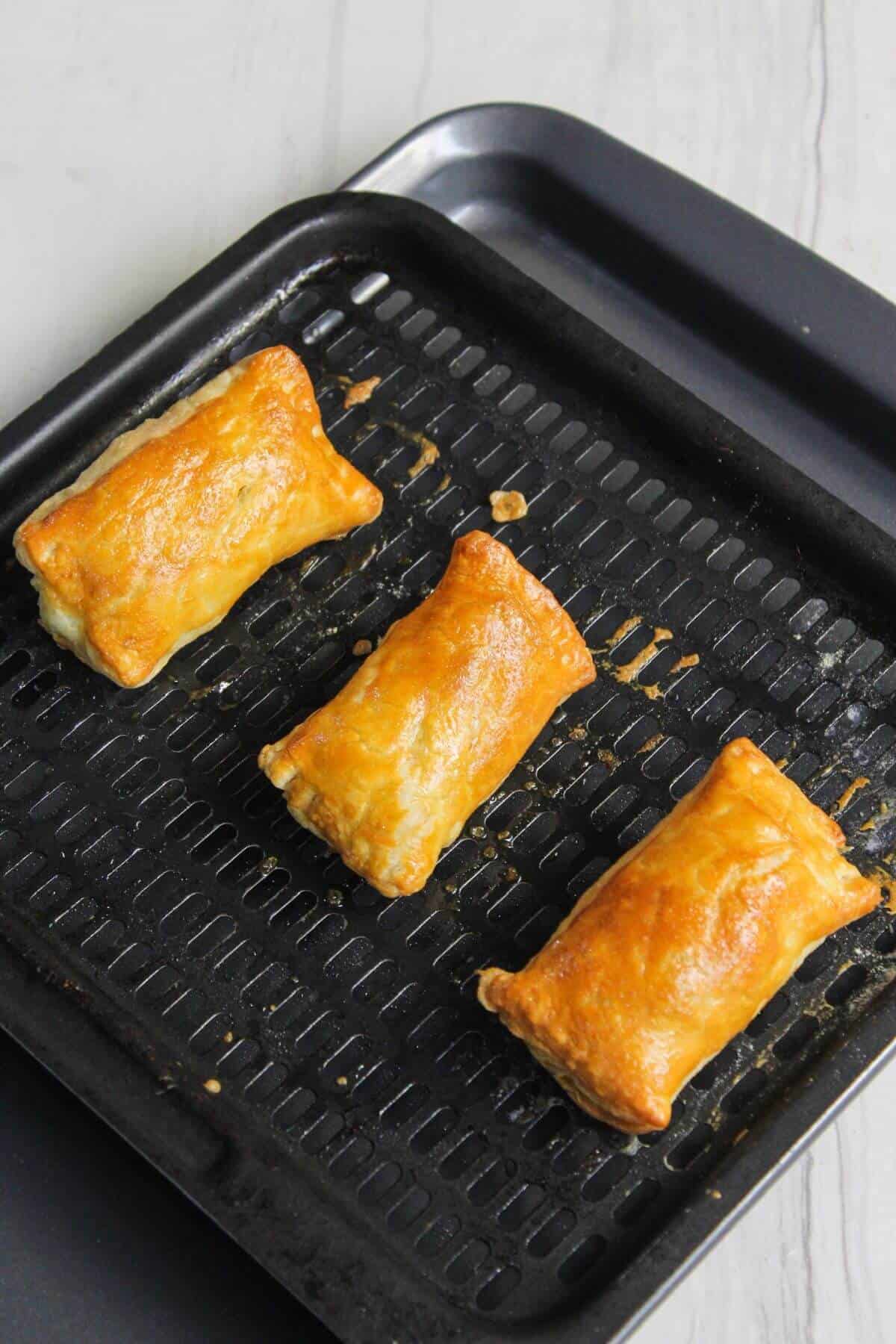 Three golden-brown pastry rolls on a black baking tray.