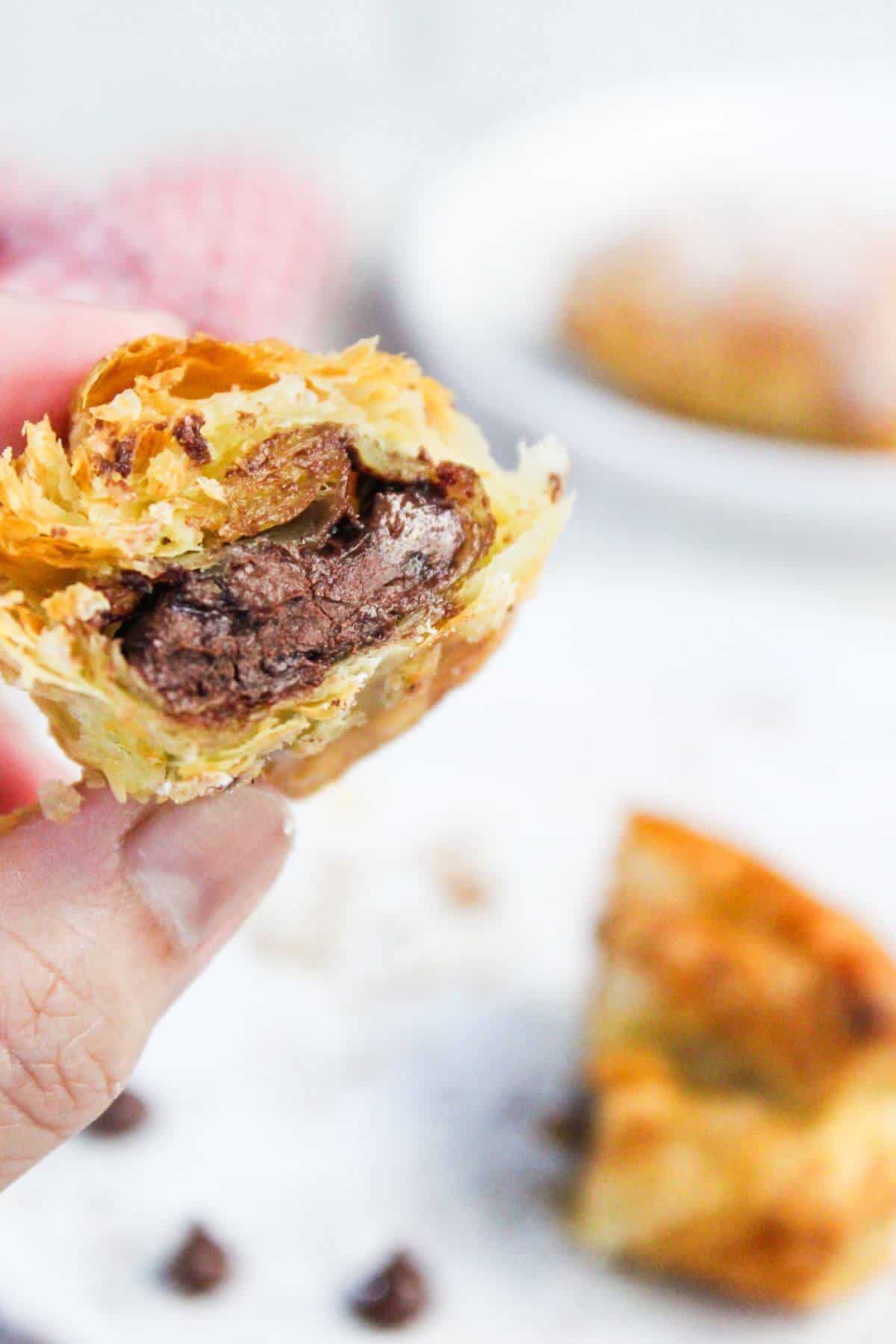 A hand holding a half-eaten chocolate-filled pastry, with more pastries blurred in the background.