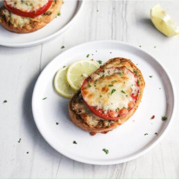 Open-faced crab melt sandwiches garnished with herbs, served with lemon slices on a white surface.