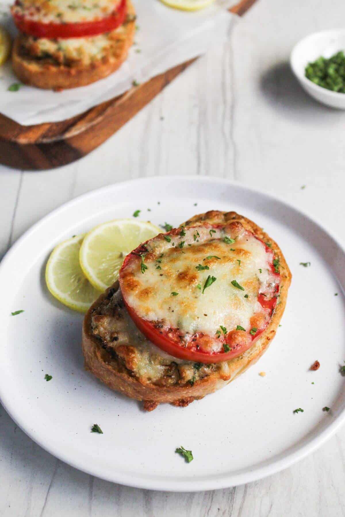 A plate with a crab melt topped with melted cheese, tomato, and herbs.