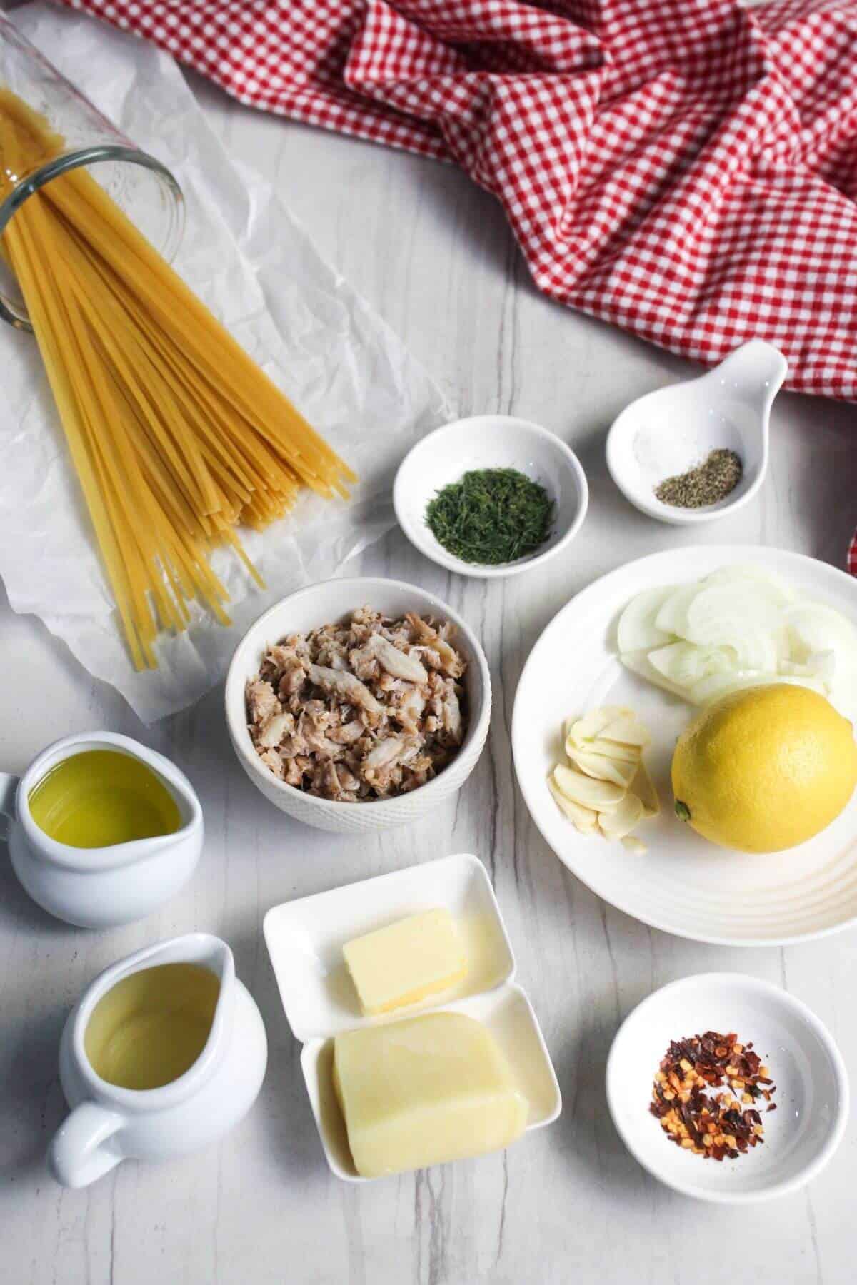 Ingredients for cooking arranged on a table, including crab, pasta, garlic, lemon, onions, butter, and spices.