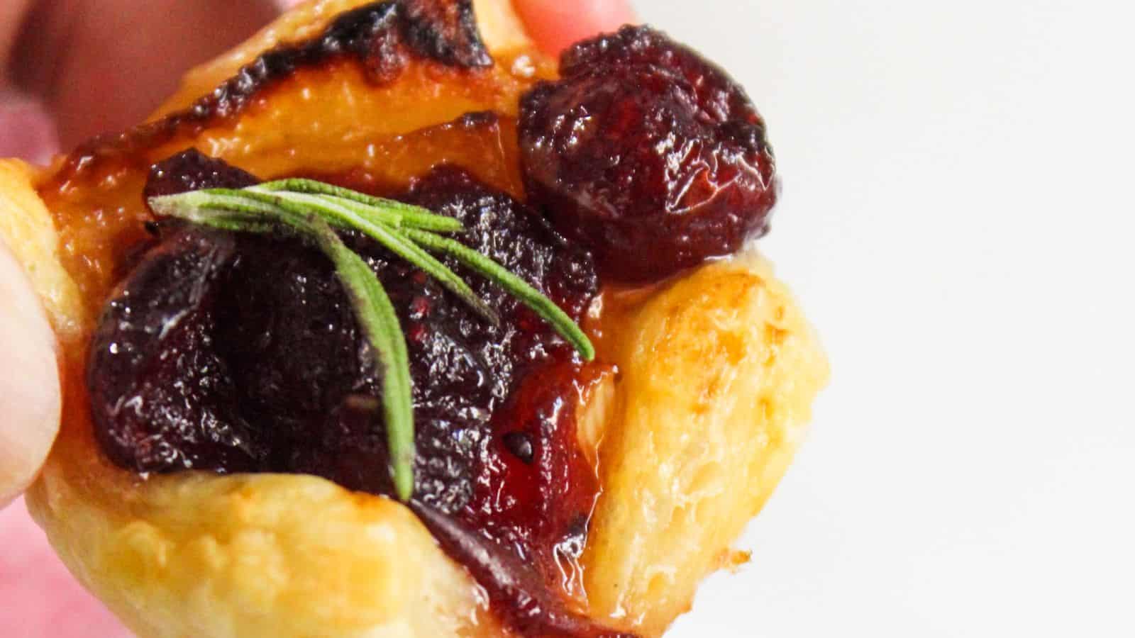 Close-up of a pastry topped with cranberries and a sprig of rosemary.
