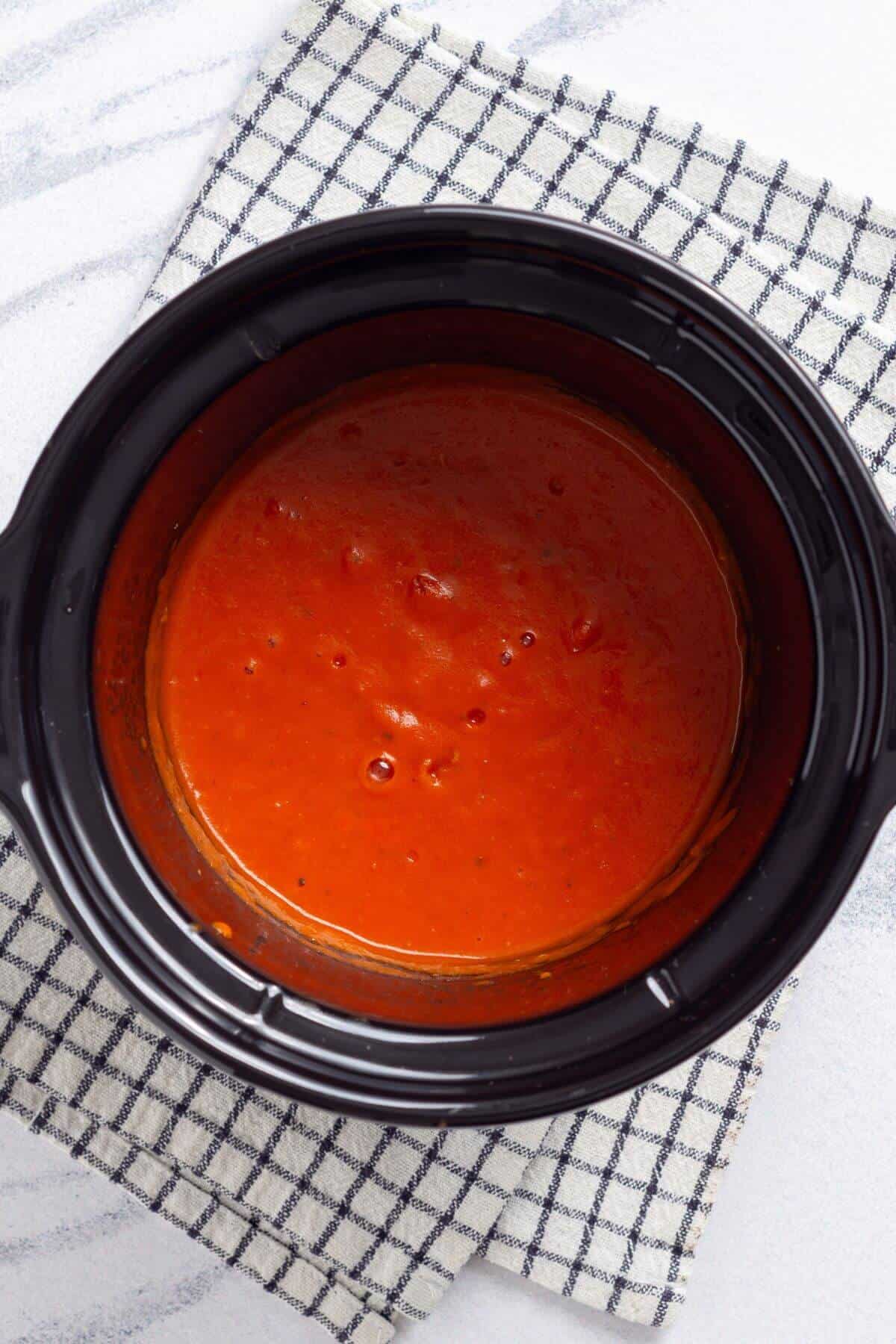 Tomato soup in a black slow cooker on a checkered cloth.