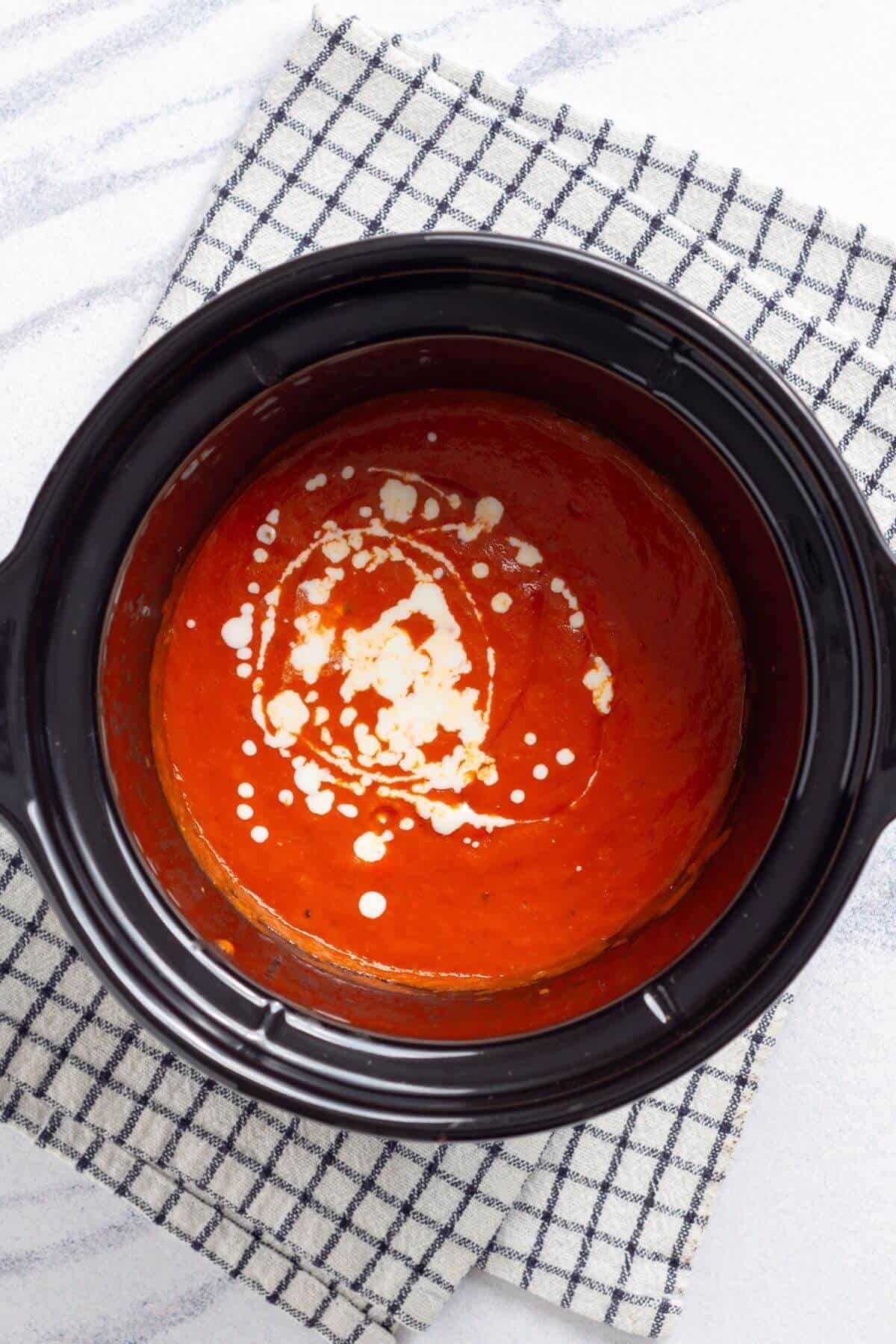 A bowl of tomato soup with a swirl of cream, on a black and white checkered napkin.