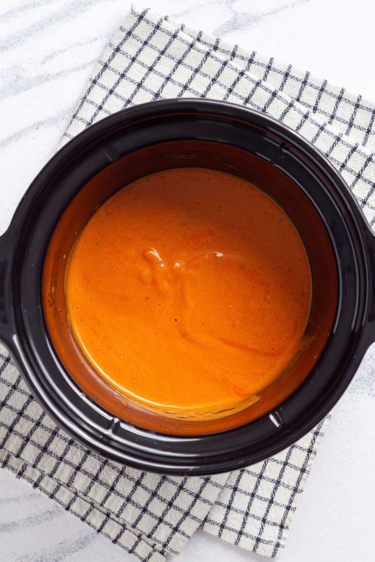 A crock pot of tomato soup on a checkered napkin.