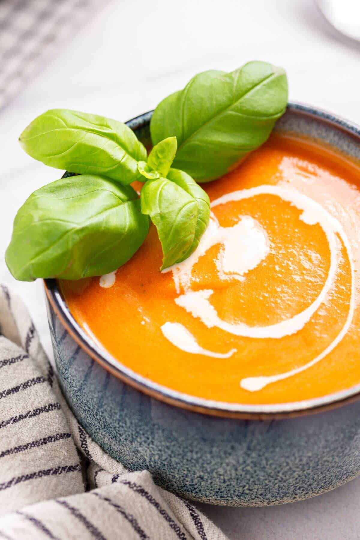 A bowl of creamy tomato soup garnished with fresh basil leaves.