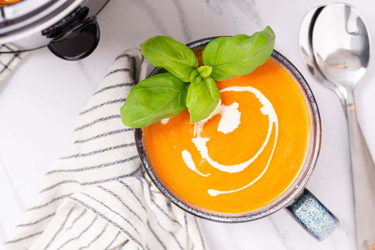 A bowl of creamy tomato soup garnished with fresh basil on a striped napkin.