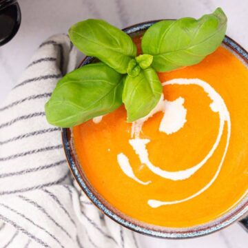 Bowl of creamy tomato soup garnished with basil leaves.