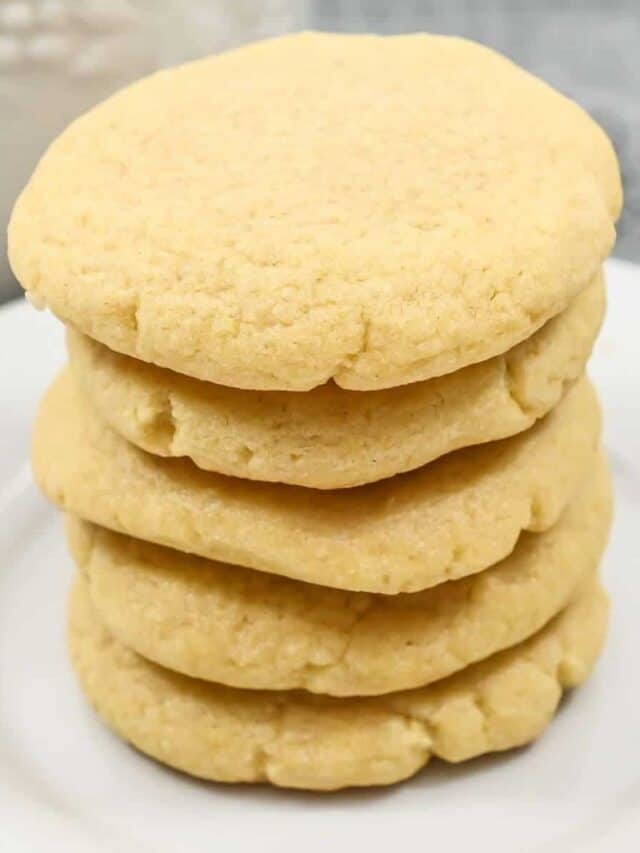 A stack of five round, golden sugar cookies on a white plate, showcasing their textured tops and soft edges.