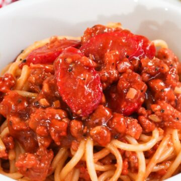 A bowl of spaghetti topped with a rich meat sauce placed on a red and white checkered tablecloth.