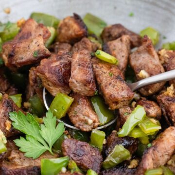 Sautéed diced meat with green peppers and herbs in a pan.