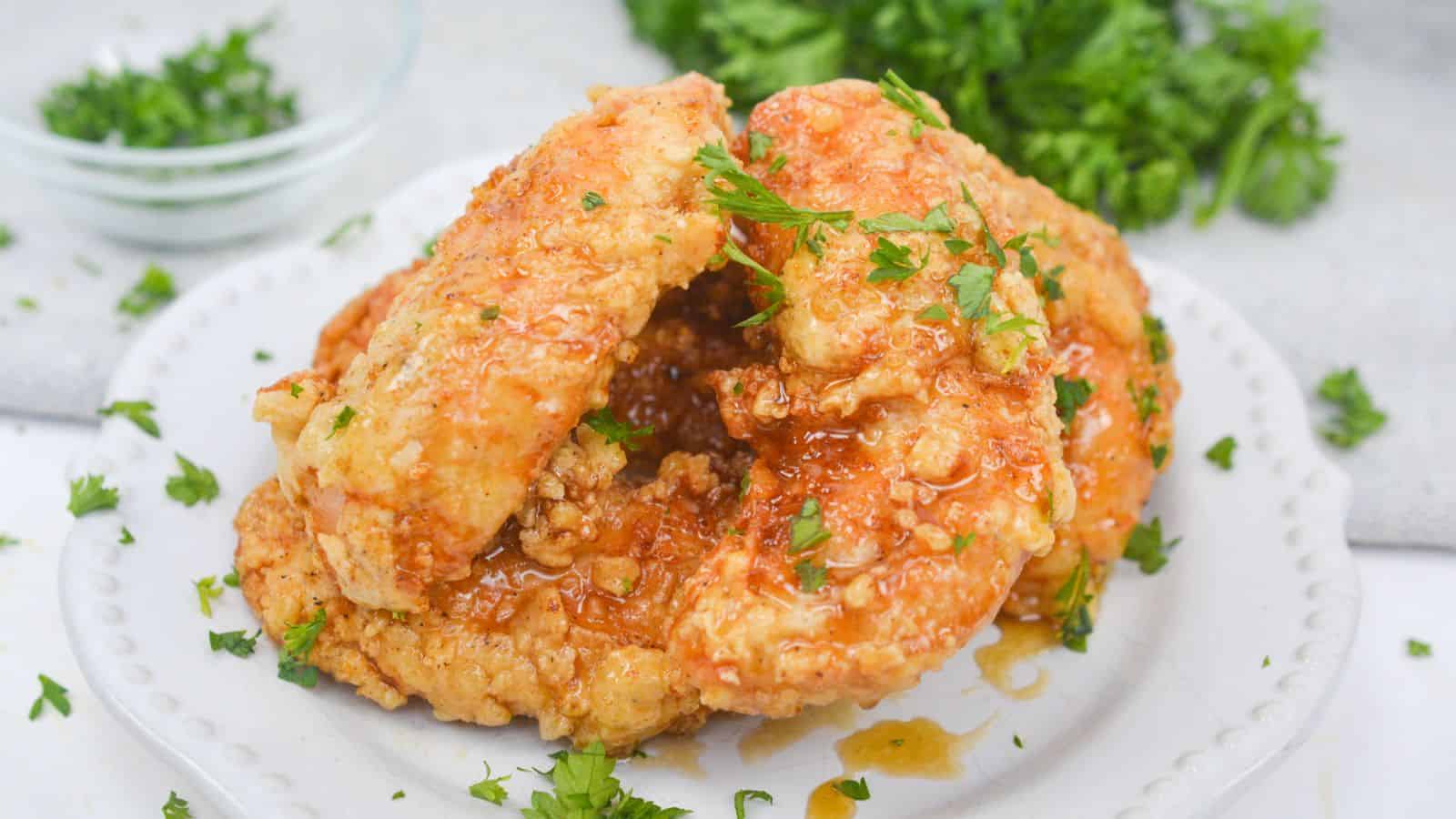 Fried chicken with honey glaze garnished with parsley on a white plate.