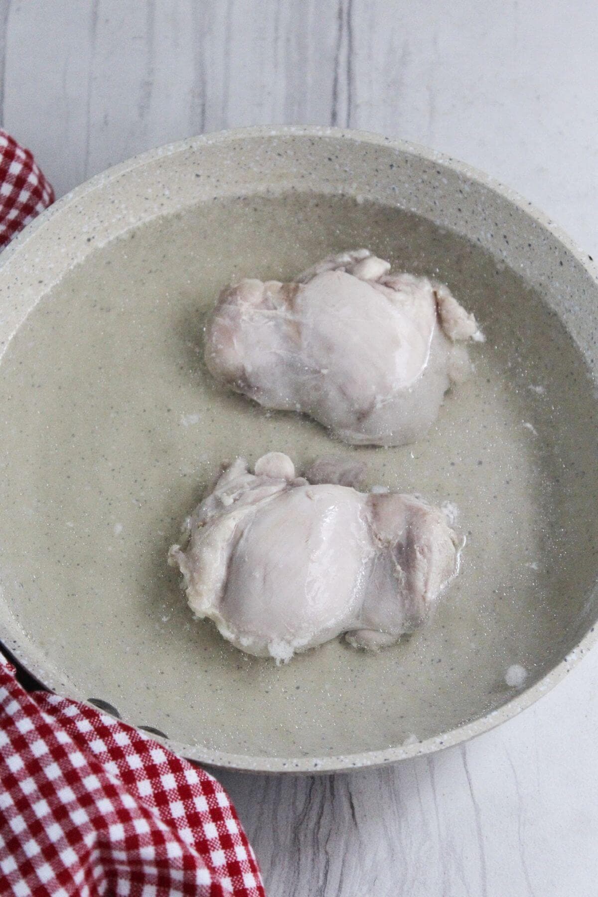 Two pieces of chicken thigh filets in a pan of water.
