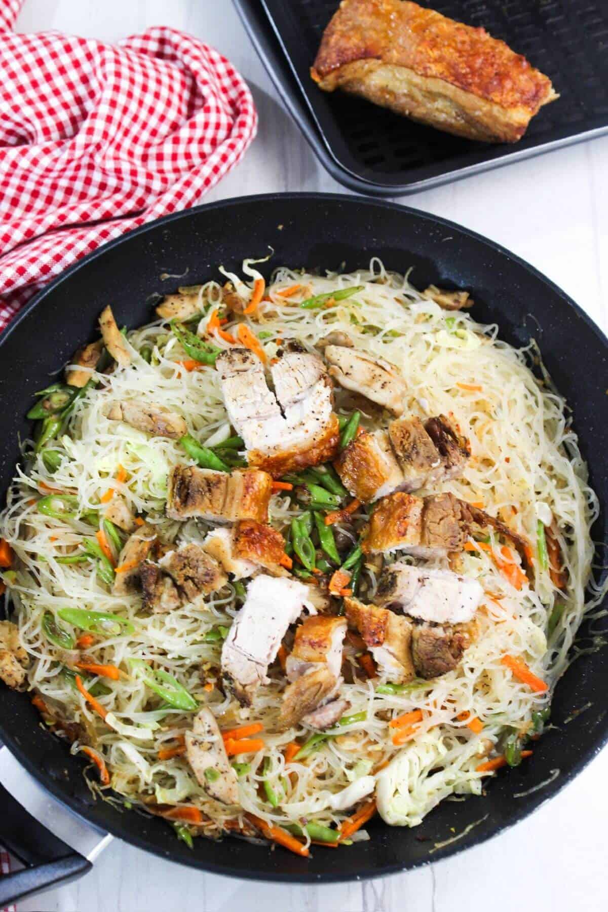 A pan with noodles and chicken in it topped with pork.
