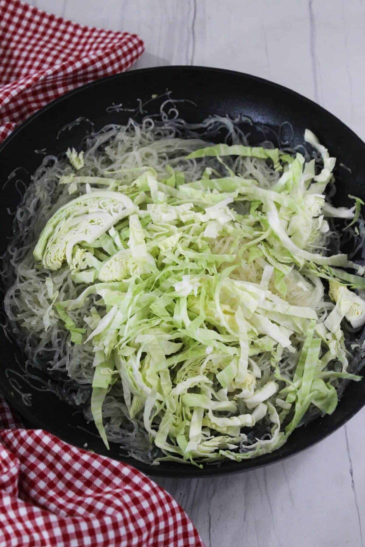 Cabbage and rice noodles in a frying pan.