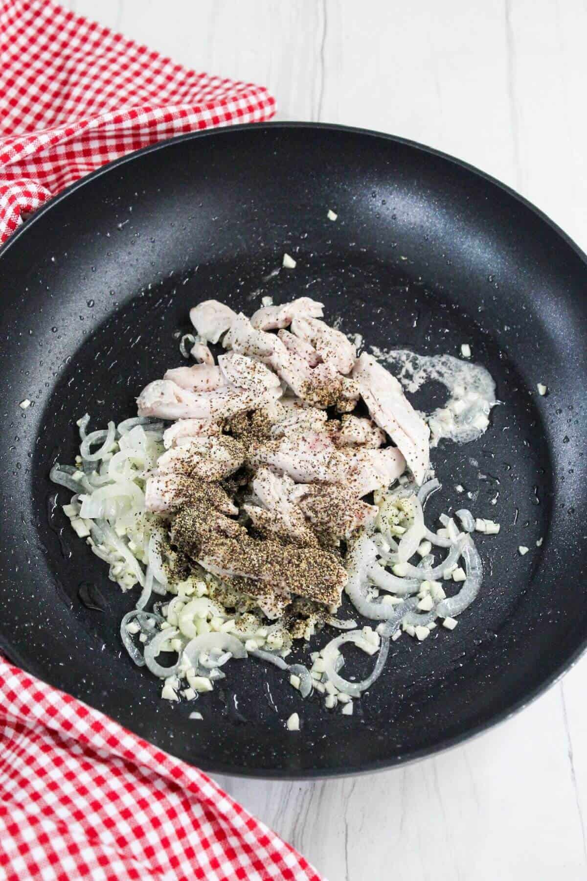 A black frying pan with onions and chicken in it.