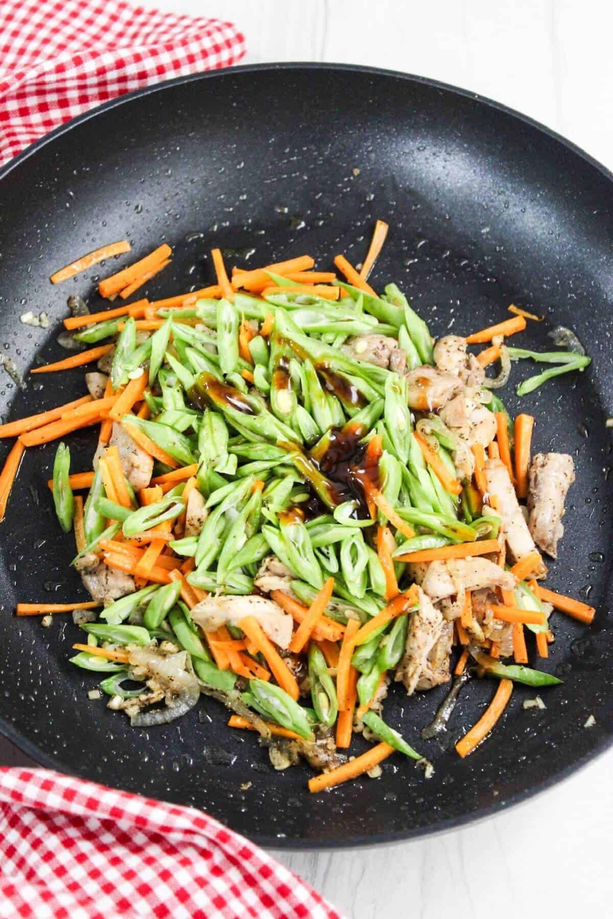 A frying pan with carrots, green beans, and chicken in it.