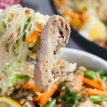 A fork twirling pancit bihon with chicken and vegetables, suggestive of a healthy meal.