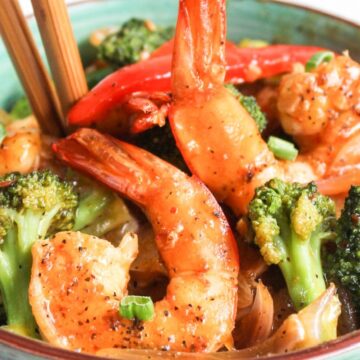 Bowl of stir-fried shrimp and broccoli with chopsticks.