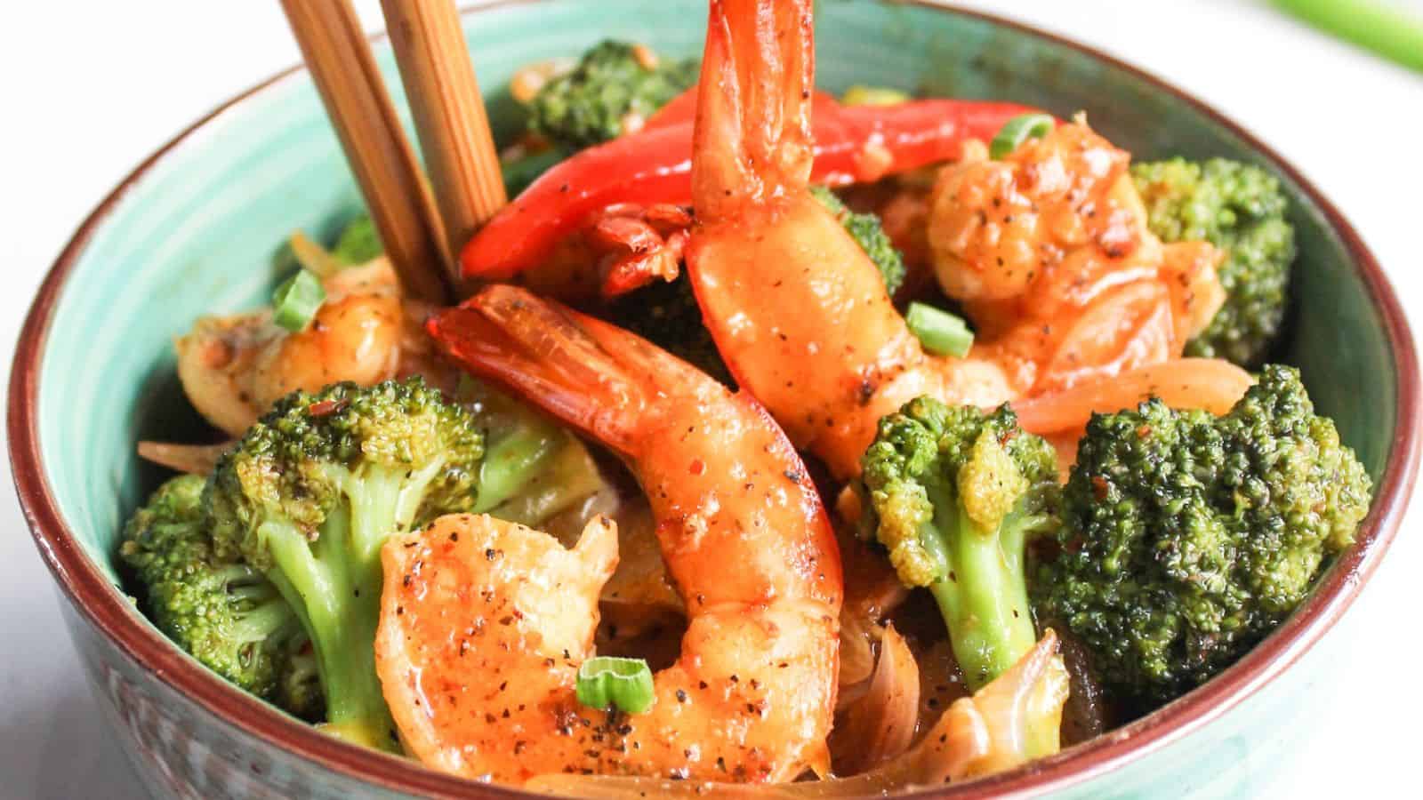 Bowl of stir-fried shrimp and broccoli with chopsticks.