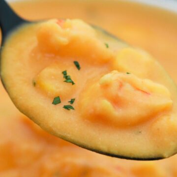 A close-up image of a spoonful of creamy shrimp bisque garnished with herbs, hovering above the rest of the soup in a bowl.