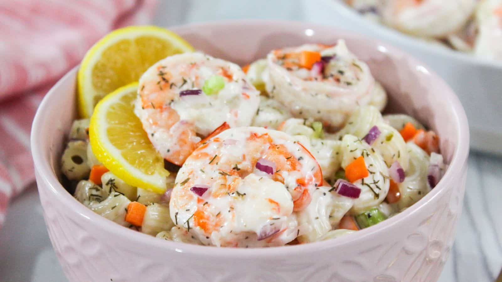 Shrimp macaroni salad in a pink bowl with lemon wedges.