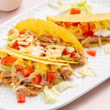 Three chicken tacos with cheese, lettuce, and diced tomatoes on a white plate.
