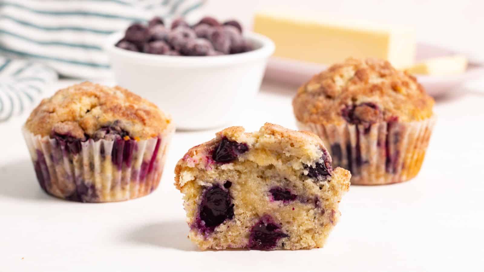 Three blueberry muffins with front one cut in half.
